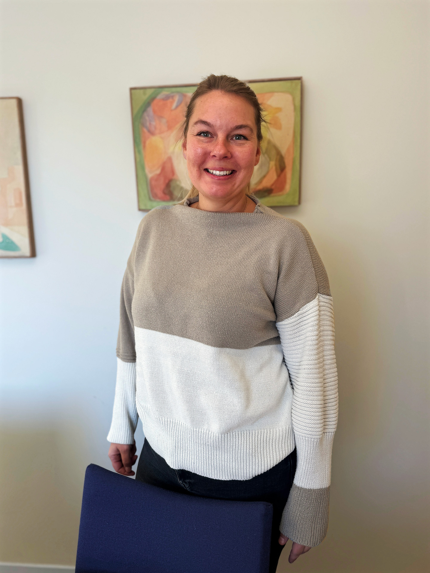 Porträttfoto, Alexandra Norelius står framför en vägg med tavlor inne i en byggnad på Solberga by.