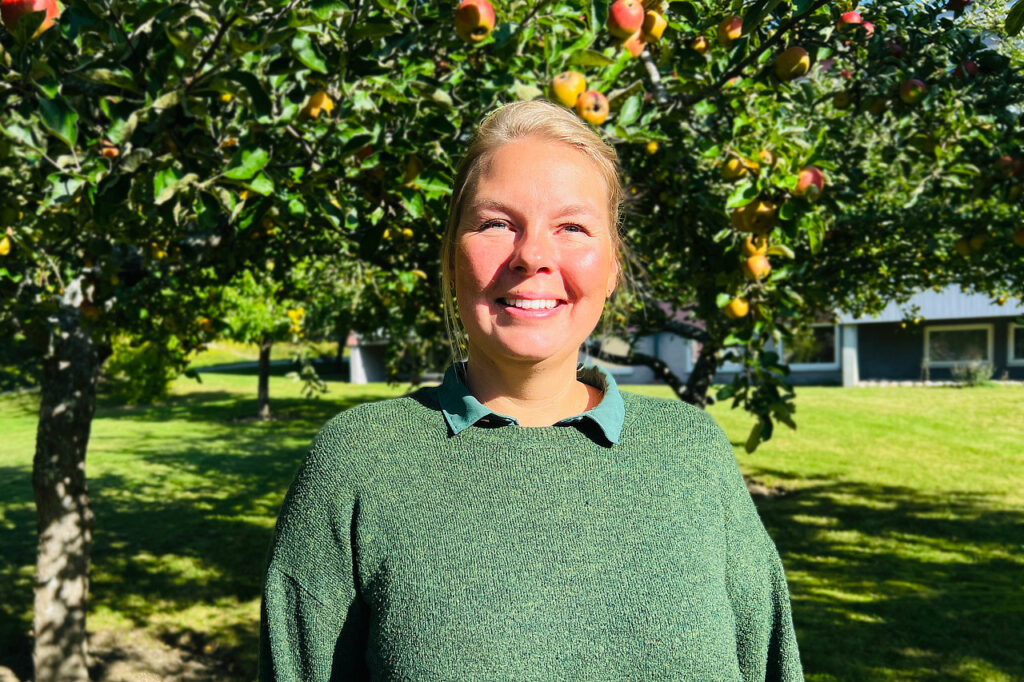 Porträttfoto, Alexandra Norelius står bland äppelträden på Solberga by.