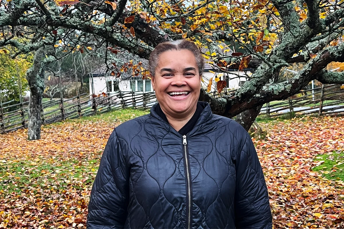 Porträtt på en leende Joana Nilsson, lärare på Solberga by, under ett äppelträd en höstdag med löv på gräsmattan.